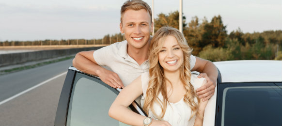 smiling couple posing beside their new car