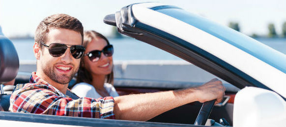 happy young couple enjoying road trip in their car hire while both looking at the camera and smiling