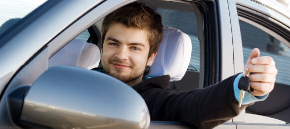 young male on a business trip showing the key of his rental car